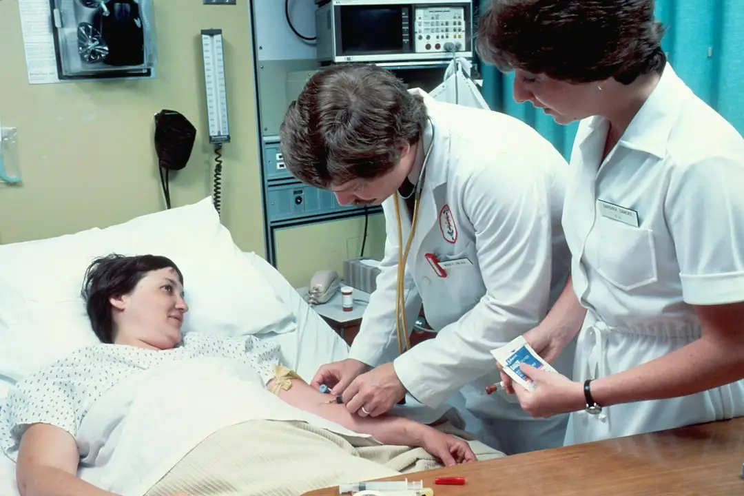 A patient in a hospital bed with a support person beside her, helping with patient safety