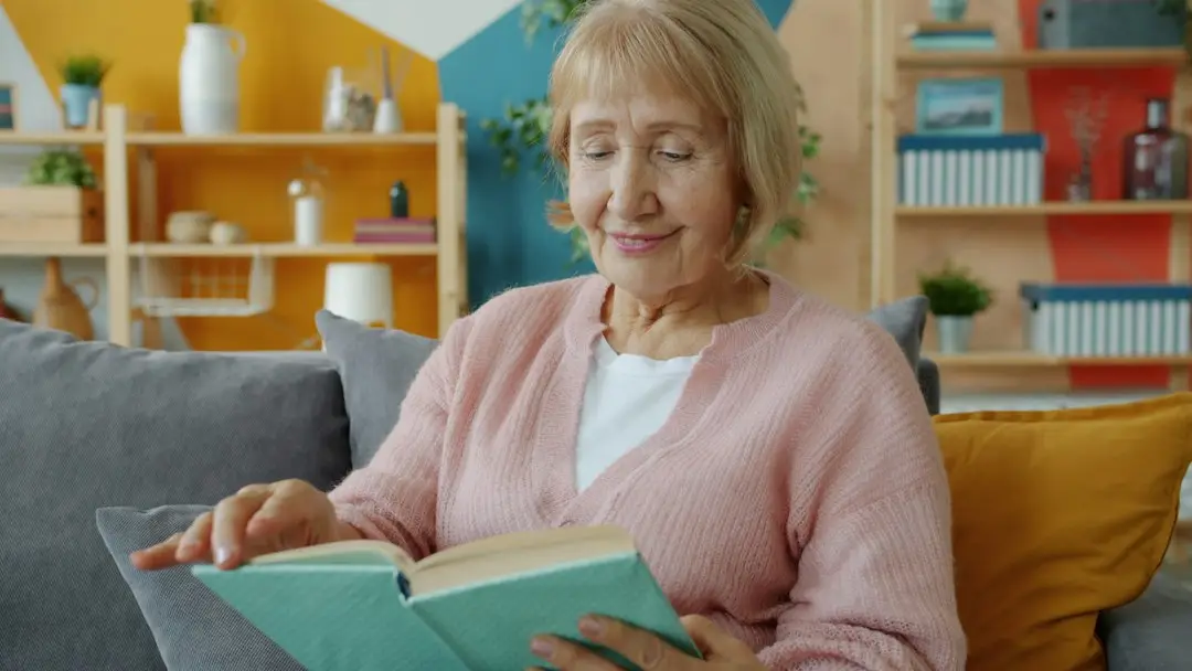 An older woman reading at home on her couch, aging alone with a plan